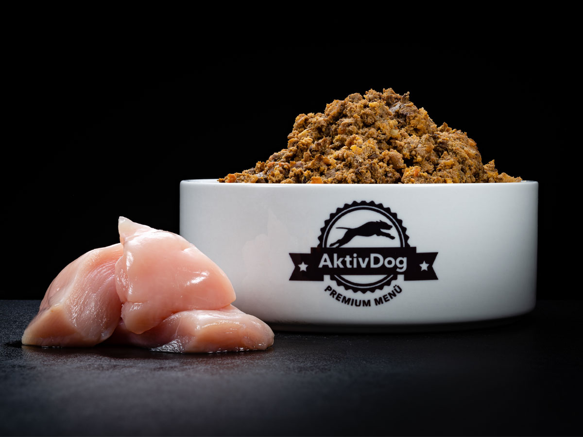 Großaufnahme von AktivDog Hundefutter Geflügel mit links daneben liegendem aufgeschnittenen Schweizer Poulet