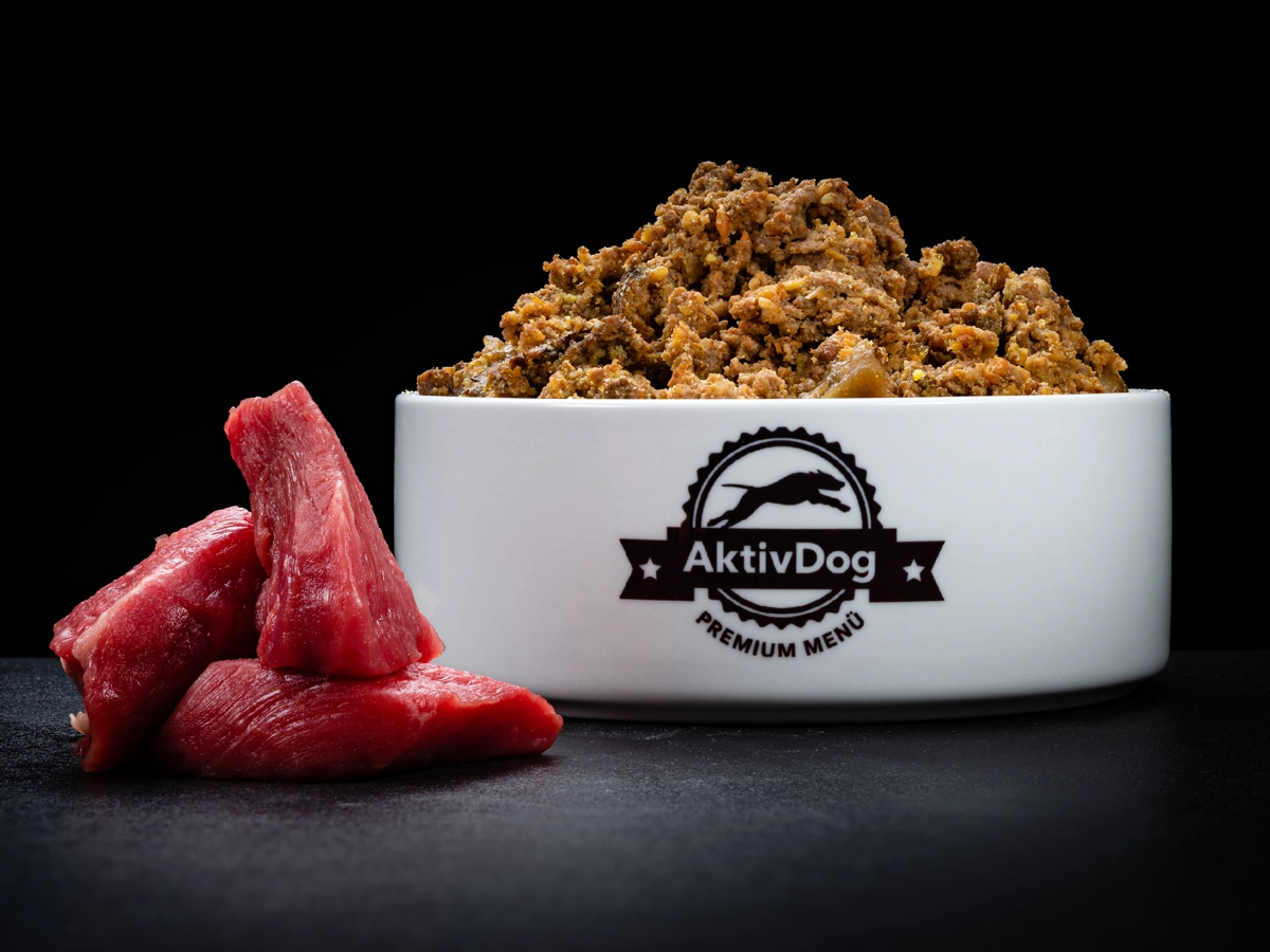 Großaufnahme von AktivDog Hundefutter Rind mit links daneben liegendem rohen Schweizer Rindfleisch