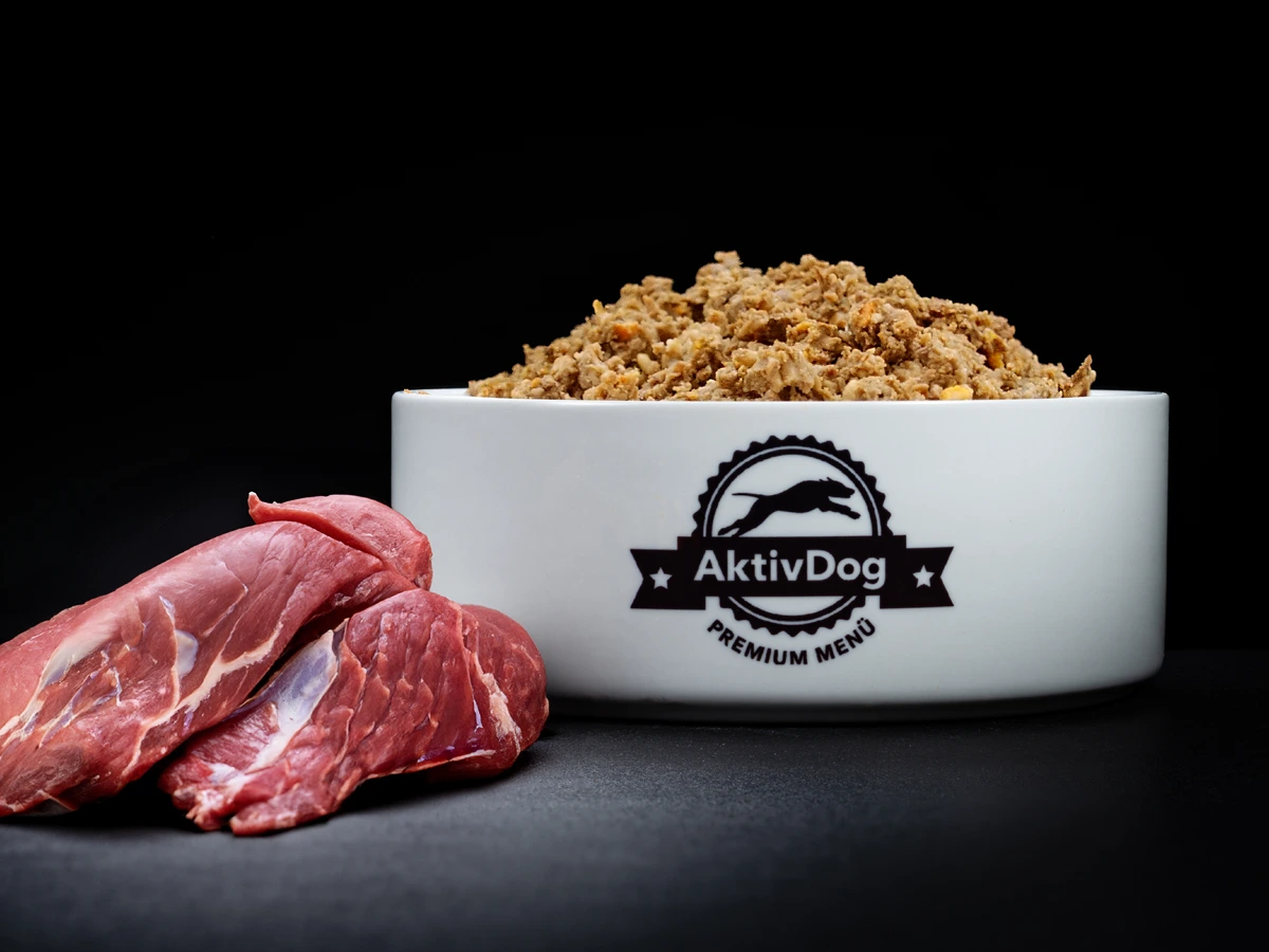 Großaufnahme von AktivDog Hundefutter Wildschwein mit links daneben liegendem rohen Wildschweinfleisch