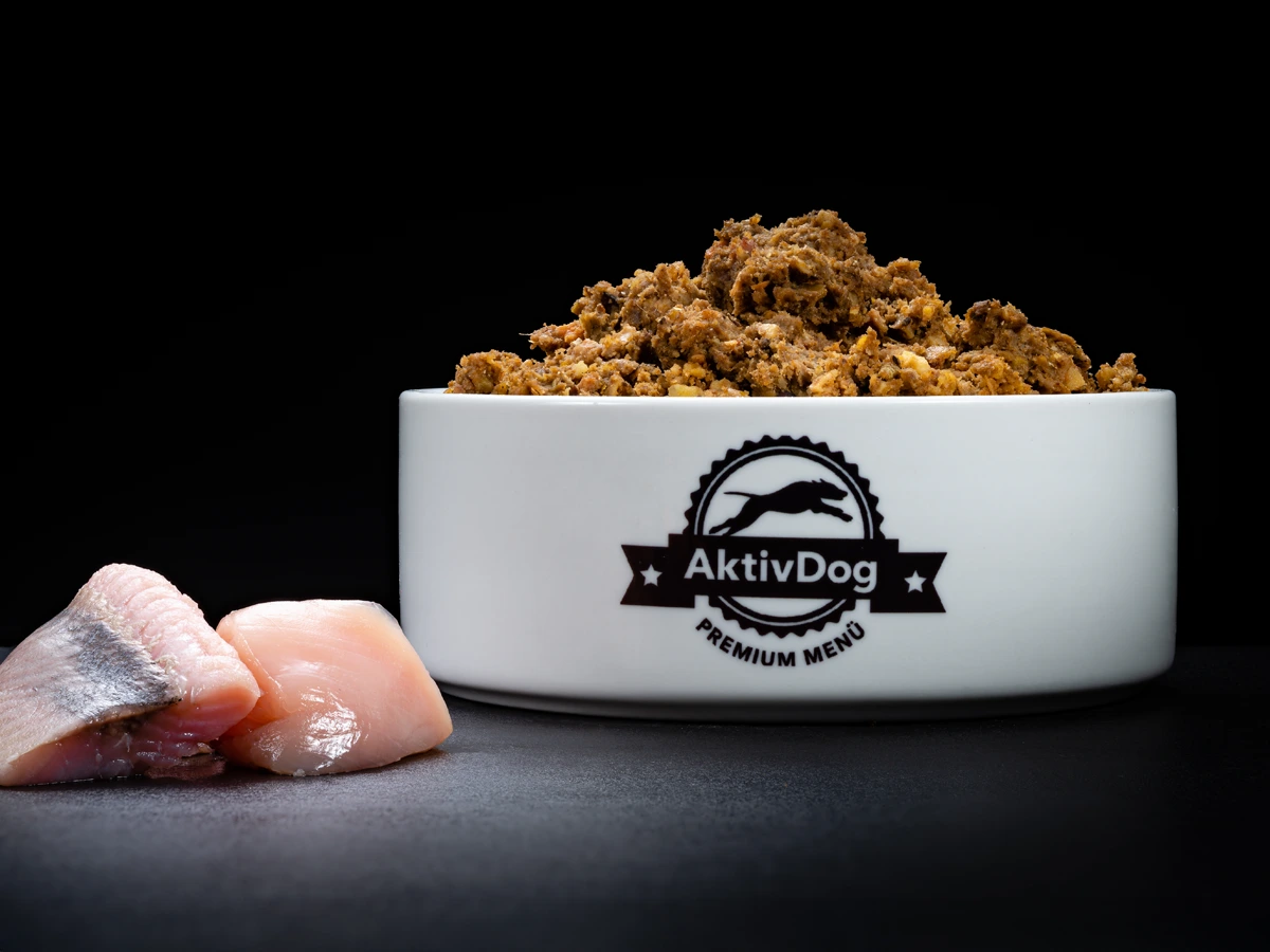 Großaufnahme von AktivDog Leistungsfutter mit links daneben liegendem rohen Schweizer Huhnfleisch und Heringfleisch